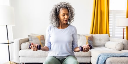 Senior woman lifting weights in living room.